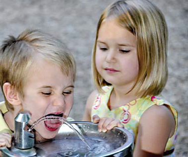 Das Foto zeigt 2 Kinder, die an einem Brunnen Wasser trinken 